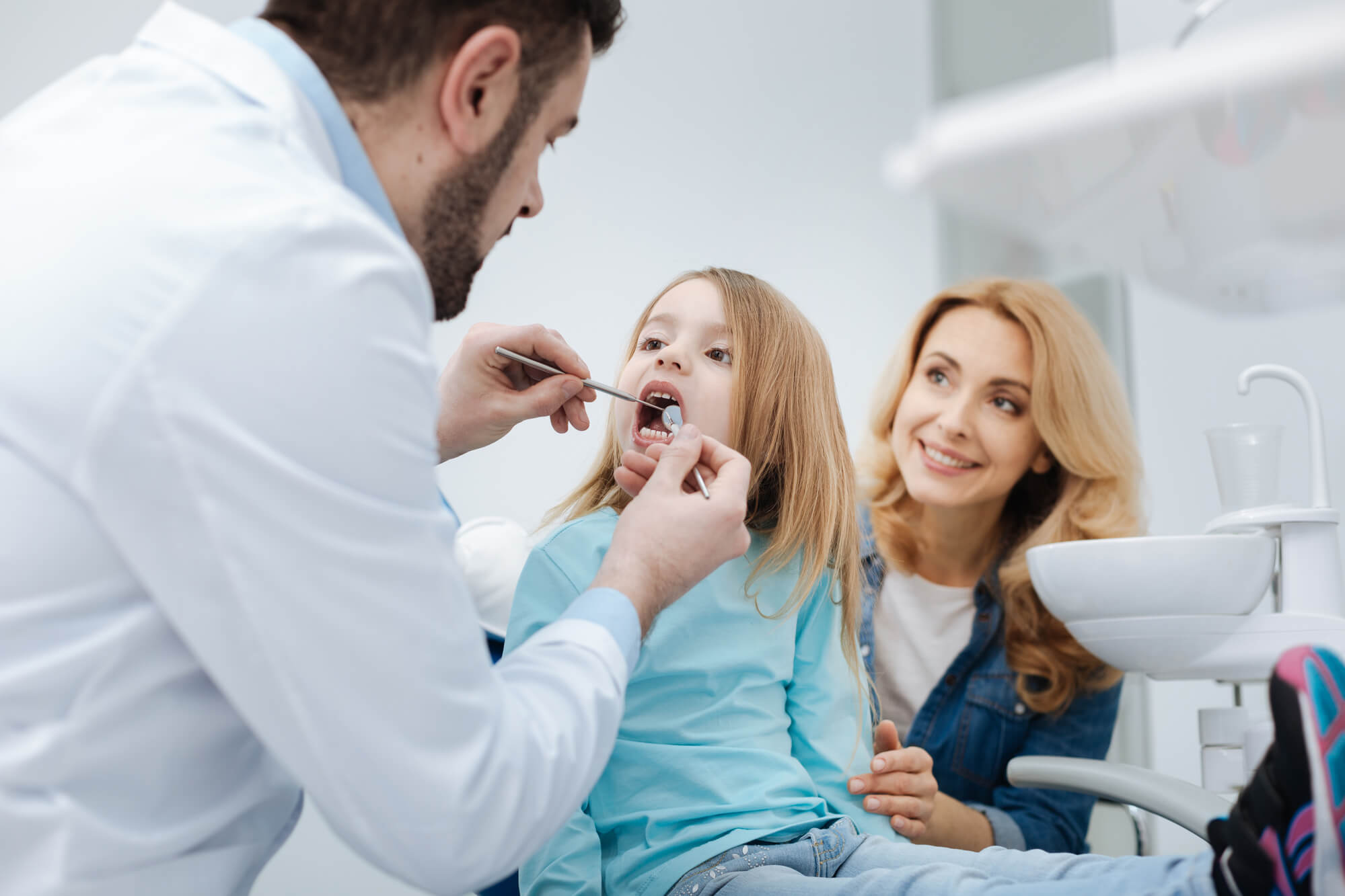 A Pediatric Dentist in Raleigh examines a little girl's teeth while her mother looks on