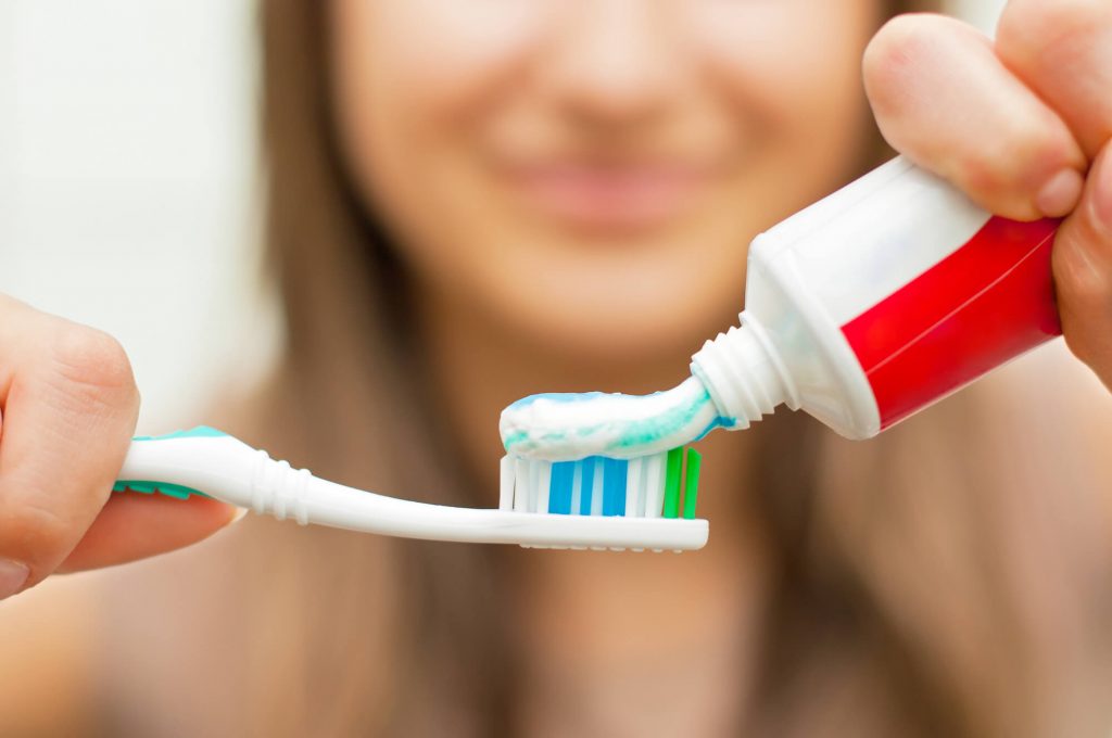 woman putting toothpaste on her toothbrush as instructed by her dentist in Zebulon