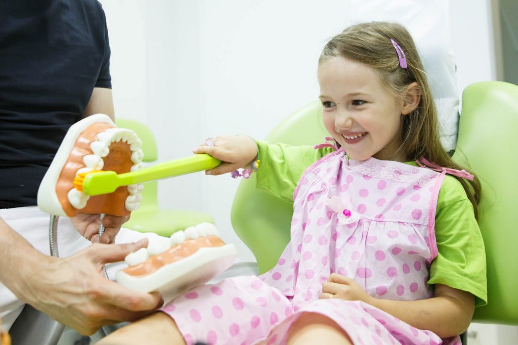 pediatric dentist in Zebulon showing a girl the proper way to brush teeth